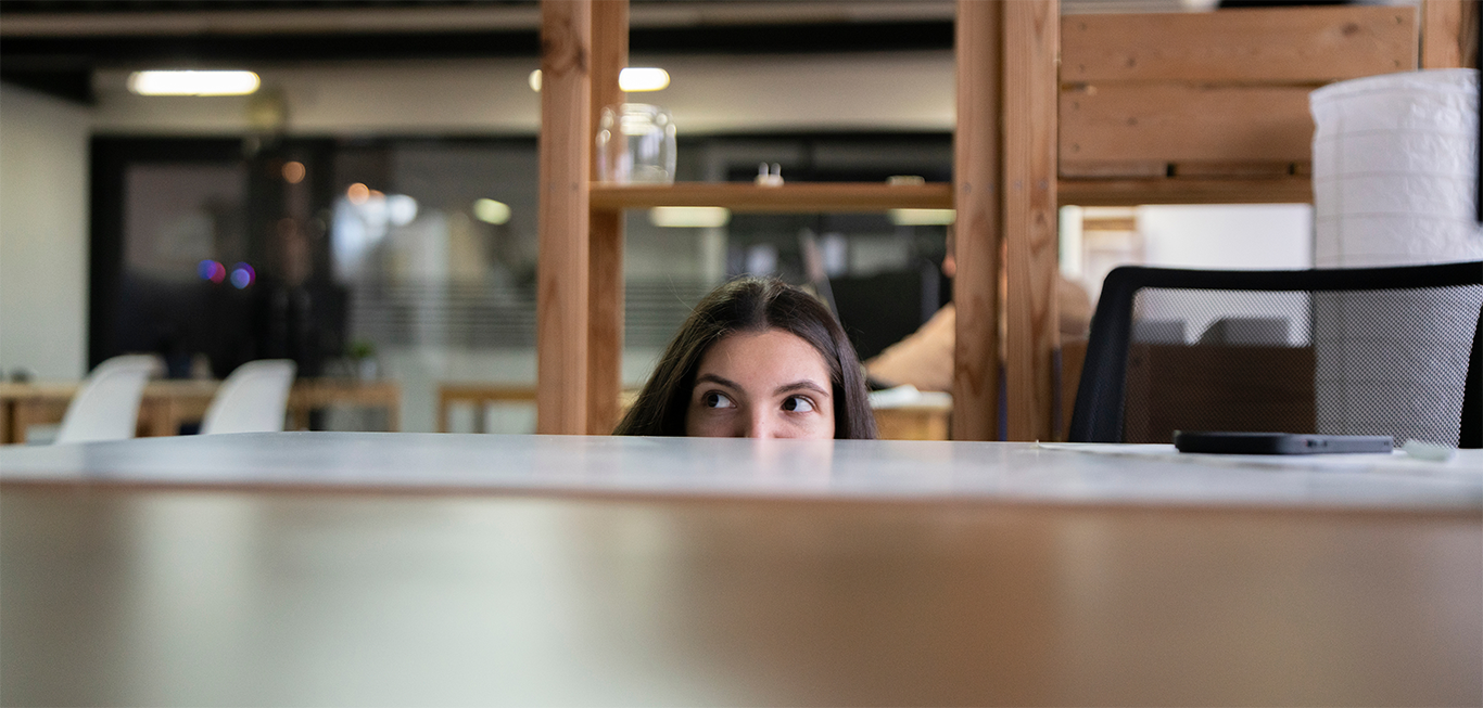 Image of woman peeking out from behind desk to support stealth mode startup strategy article