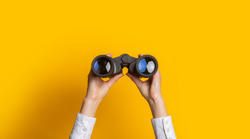 Person holding up binoculars against a yellow background to support talent shortage article