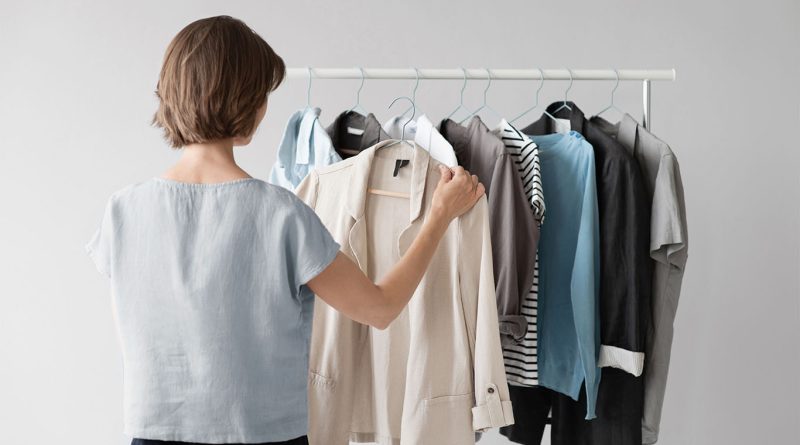 Woman selecting a beige blazer from a minimalist clothing rack with various business casual tops and jackets