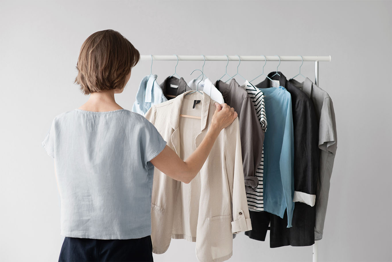 Woman selecting a beige blazer from a minimalist clothing rack with various business casual tops and jackets