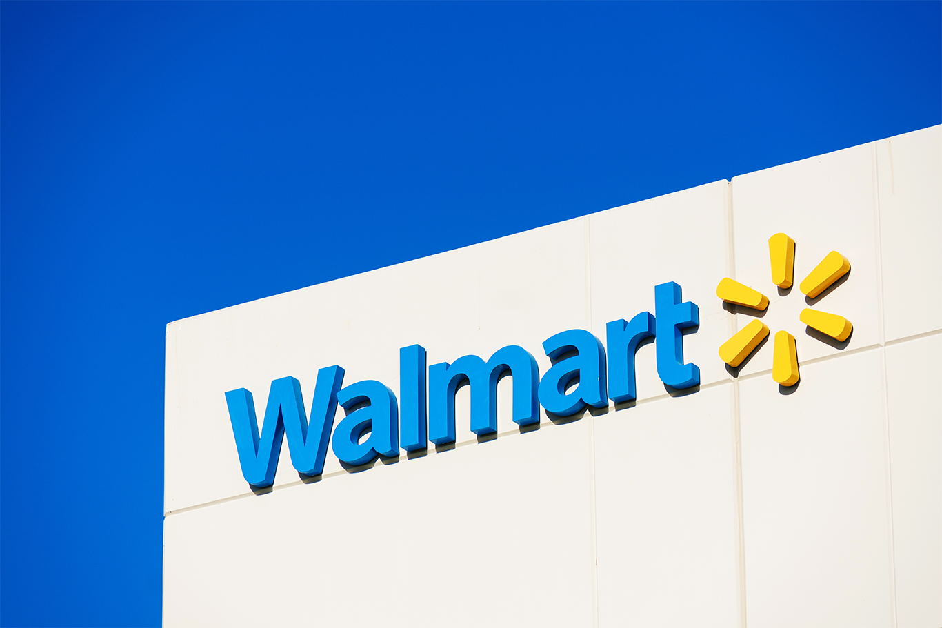 Walmart logo mounted on the exterior of a store building against a clear blue sky.